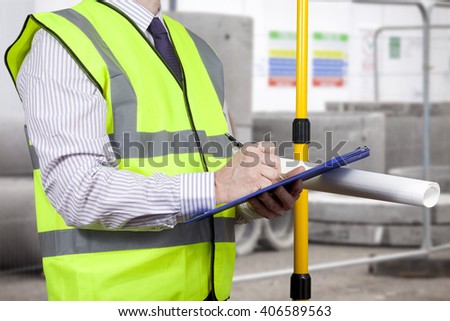Building surveyor in a high visibility vest writing on his clipboard on a construction site