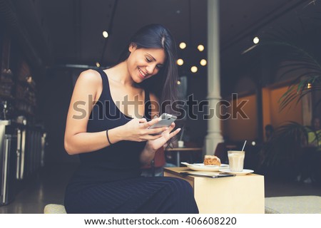 Young latin woman making self portrait on her smart phone digital camera while sitting in sidewalk cafe during lunch break. Pretty female posing while photographing herself for social network picture