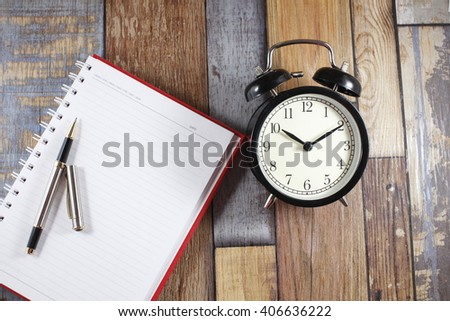 alarm clock on wooden table with book and pen