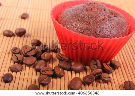 Homemade delicious fresh baked chocolate muffins in red silicone cups and coffee grains lying on wooden background, concept for dessert