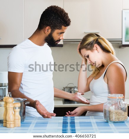 Young european interracial family couple with serious faces quarrelling in kitchen
