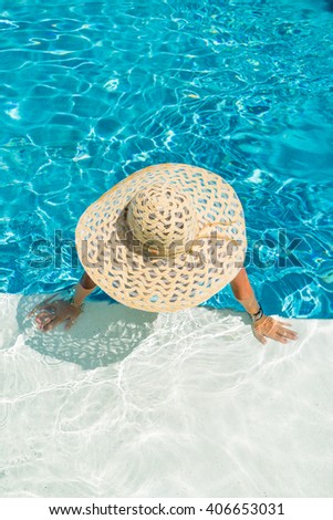 Pretty woman in a hat enjoying a swimming pool at the resort