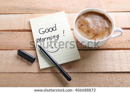 Cup of coffee and note GOOD MORNING on wooden background