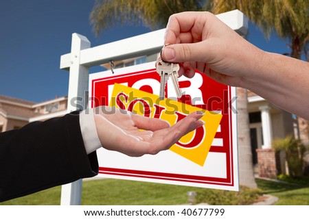 Agent Handing Over the Key to a New Home with Real Estate Sign and House in the Background.