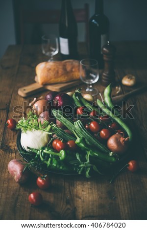Different fresh farm vegetables on wooden table. Wine bottles and bread on background. Autumn harvest and healthy organic food concept. Toned picture