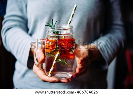 Hands holding retro glass jar of lemonade or cocktail with strawberry and rosemary. Toned picture