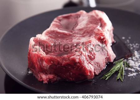 Raw pork steak with rosemary on black plate