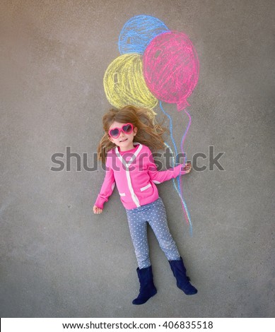 A cute little girl with sunglasses is holding creative chalk balloons drawn on the sidewalk cement for a imagination, summer or activity concept.
