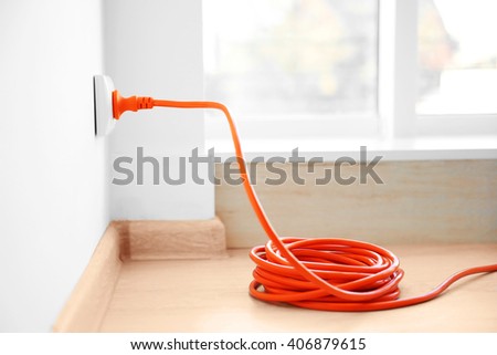 Orange extension into power outlet indoors Royalty-Free Stock Photo #406879615