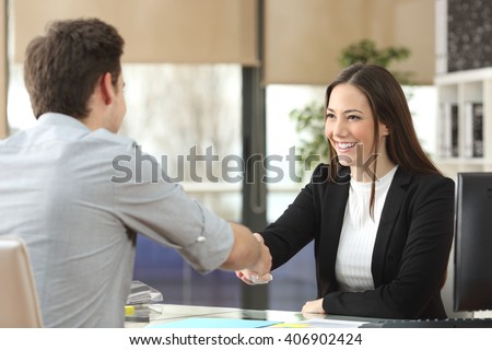 Happy businesswoman handshaking with client closing deal in an office interior with a window in the background Royalty-Free Stock Photo #406902424