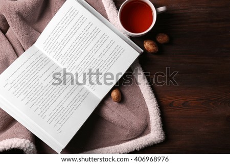 An open book, a cup of tea, nuts and a blanket on the wooden background