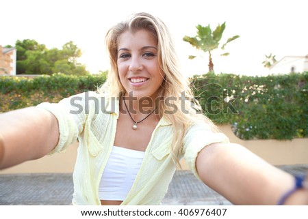 Portrait of a beautiful teenager girl holding a smart phone to network, taking selfies photos and videos in home exterior at sunset, outdoors. Technology lifestyle, adolescent smiling at camera.