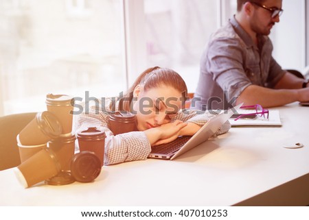Portrait of tired freelance lady sleeping on laptop computer while many cups of coffee near by her. Pretty lady resting after hard working day. Toned picture. 