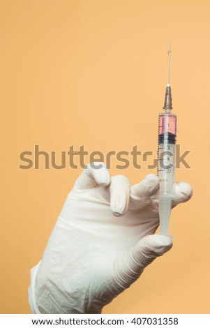 Close up of female doctor's hand in white sterilized surgical glove with plastic medical syringe filled 