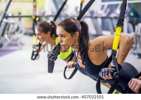 Women training arms with trx fitness straps in the gym doing push ups train upper body chest shoulders pecs triceps. Royalty-Free Stock Photo #407032501