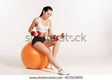 Young beautiful sportswoman with dumbbells exercising on fitball