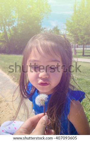 A lovely little girl learning how to blow dandelion in mommy's hand at public park ,filtered color tone in picture.