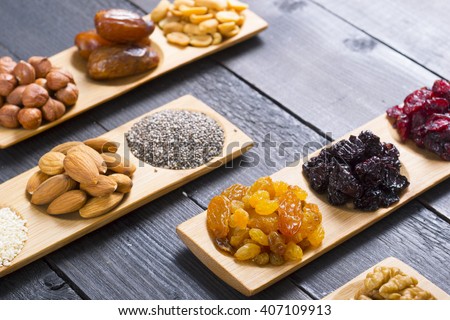 sun dried berry fruits, nuts and seeds on bamboo serving trays, black wood table background