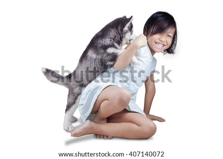 Picture of a joyful little girl playing in the studio with siberian husky puppy, isolated on white background