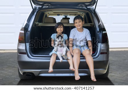 Picture of two happy children sitting in the car while holding husky dog and smiling at the camera