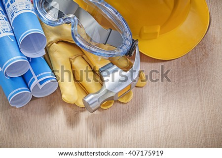 Protective workwear claw hammer rolled construction drawings on wooden board.