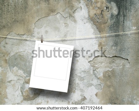 Close-up of one blank square instant photo frame hanged by peg against cracked concrete wall background 