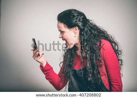 young woman screaming on the phone, wearing a overalls, close-up isolated on a gray background