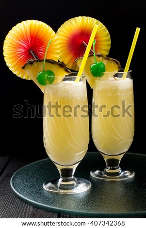 Refreshing pineapple cocktail with coconut in glasses with slices of pineapple, green cocktail cherry, straws and decoration for glasses in the form of a fan