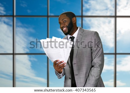 Smiling black businessman holds contracts. Friendly official on sky background. Sign and join the team. Your next step towards success.