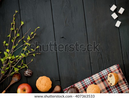 Cupcakes on a plate, red apple, wooden spoon, black coffee, refined sugar, chocolate, light breakfast. Black wooden table. Green fresh leaves.