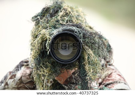 wildlife photographer using camouflage and pointing his huge 300mm 2.8 lens at you while outdoors