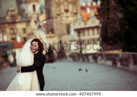 Romantic strong newlywed groom carrying happy bride on bridge in Prague