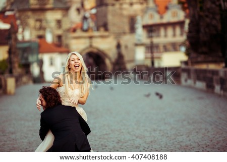 Romantic strong newlywed groom carrying happy bride on bridge in Prague