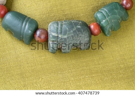Ancient elephant beads separated with ancient carnelian beads on green Thai silk background