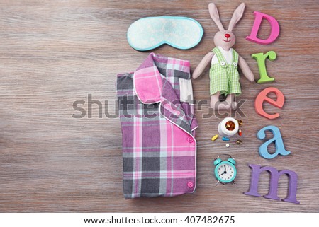 Word Dream with little toy, pajamas and mask on a wooden background