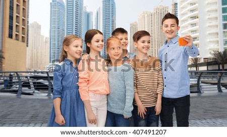childhood, friendship, technology and people concept - group of happy children talking selfie by smartphone over dubai city street background