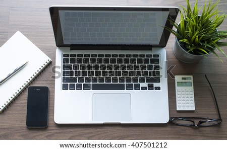 Top view of laptop with smartphone ,blank notebook,calculator and small green plant  