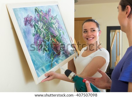 Positive smiling couple hanging picture in frame on the wall
