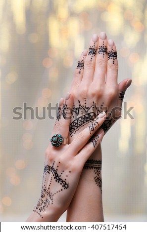 Female hands with henna tattoo on bright blurred background