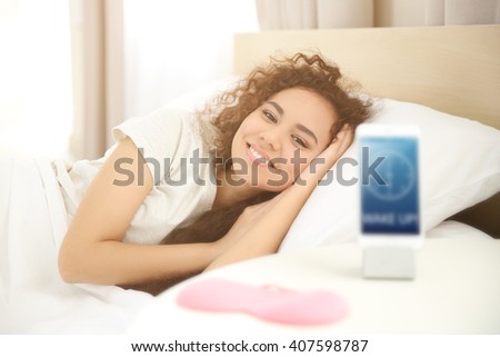 Awake girl and alarm clock in bedroom
