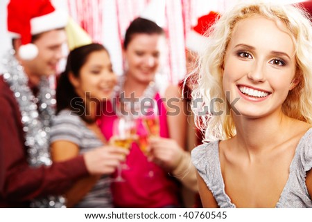 Face of pretty girl looking at camera with smile on background of her friends partying