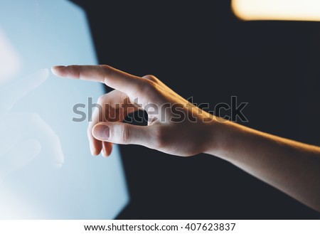 Closeup of a man pointing finger to screen with a blank screen monitor in the hands, working behind a computer keyboard and blue monitor in the night in the office horizontal Royalty-Free Stock Photo #407623837