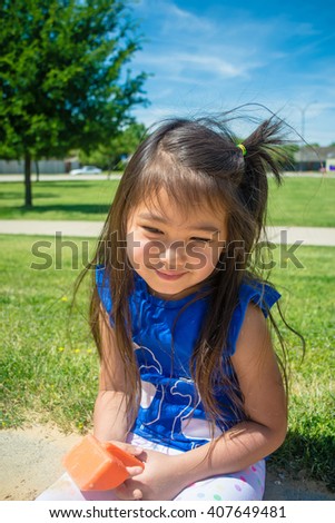 A closed up of little girl smiling and playing sand at public park  with blue sky background,filtered color tone in picture.