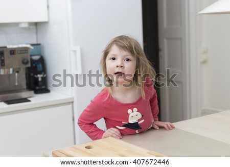 a small blond scandinavian girl making grimace and standing close to the kitchen table at home