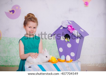 Little girl in a green dress in studio stroking the little white rabbit