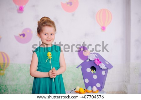 Little girl in a green dress in studio is holding a wooden egg