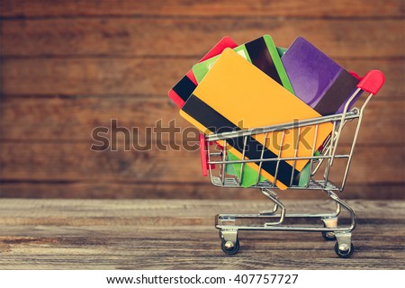 Shopping cart with credit cards on old wood background. Toned image.