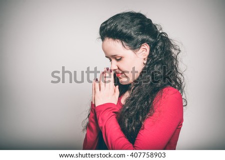 Young woman points praying, religion theme, dressed in a overalls, close-up isolated on a gray background