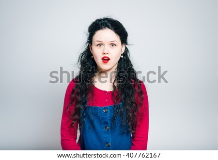 surprised young woman, opened her mouth, wearing a overalls, close-up isolated on a gray background