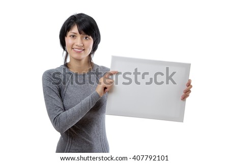 Upper body shot of a slim young female fitness model, wearing a long sleeved grey top, holding a blank white board. 